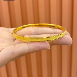 Pode incluir: Uma pulseira de ouro com uma faixa central texturizada. A pulseira &eacute; de cor dourada brilhante e parece ser feita de metal. A pulseira &eacute; redonda e lisa nas bordas.