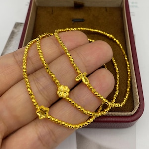 May include: Three gold bracelets with different charms: a star, a four-leaf clover, and a cross. The bracelets are made of small, faceted beads. The bracelets are displayed in a brown jewelry box with a red interior.