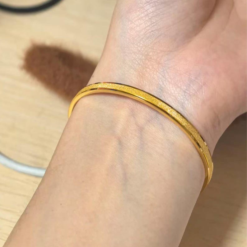 Pode incluir: Uma pulseira dourada com uma superf&iacute;cie texturizada. A pulseira &eacute; usada no pulso e tem um design simples e elegante. A pulseira tem aproximadamente 6,35 cm de di&acirc;metro.