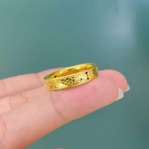 Könnte beinhalten: Ein goldener Ring mit einem Wabenmuster. Der Ring hat eine leuchtend gelbe Farbe und scheint aus Metall zu sein. Der Ring wird auf einem Finger gehalten.