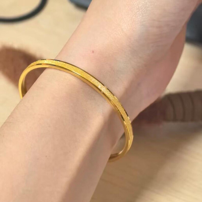 Pode incluir: Uma pulseira dourada com uma superf&iacute;cie texturizada e brilhante. A pulseira tem um design simples e elegante e &eacute; usada no pulso. A joia &eacute; um acess&oacute;rio cl&aacute;ssico.