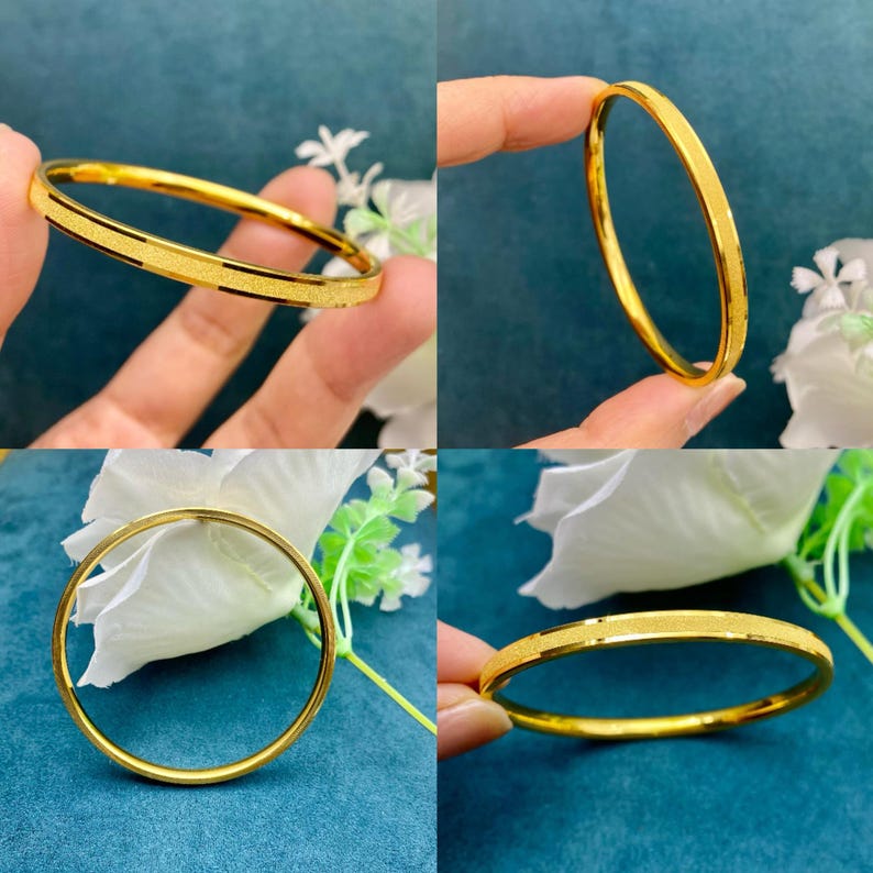 Pode incluir: Um conjunto de quatro pulseiras douradas. As pulseiras s&atilde;o redondas e t&ecirc;m uma superf&iacute;cie texturizada. Uma pulseira tem uma faixa preta. As pulseiras s&atilde;o exibidas em um fundo azul com flores brancas.
