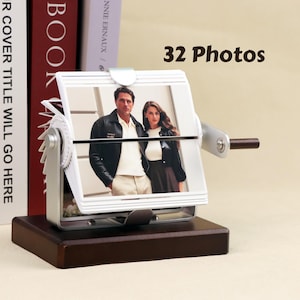May include: A silver photo album with a wooden base and a crank handle. The album holds 32 photos and features a photo of a couple on the front.