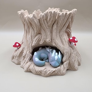 Peut inclure: Un pot de fleurs fantaisiste en forme de souche d'arbre de couleur claire avec une figurine de dragon endormi à l'intérieur. Deux figurines de champignons rouges et blancs sont fixées à l'extérieur du pot. Le dragon est bleu et blanc.