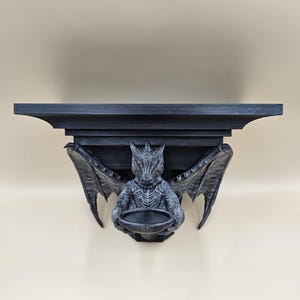 Peut inclure: Étagère murale en forme de dragon noir avec un petit bol dans ses griffes. L'étagère est en plastique imprimé en 3D et a un style gothique.