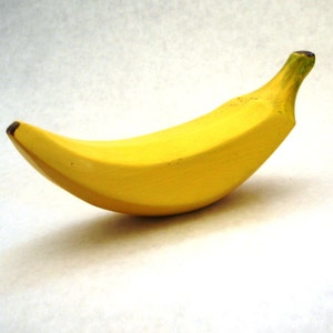 May include: A ripe banana, with a bright yellow peel and a slightly curved shape, rests on a white surface. The banana's stem is green, and the tip is brown. The fruit casts a soft shadow.