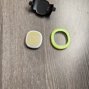 May include: A white and gold Mickey Mouse themed tracker with a black charging base and a green ring.