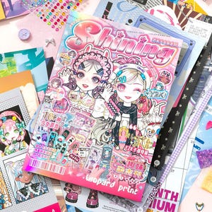 May include: A collection of colorful magazines and stickers with a pink and purple theme. The main magazine cover features two anime-style girls with the word "Shining". Other magazines and stickers are scattered around, with text like "Leopard print".