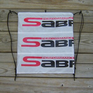 May include: White drawstring bag with three rows of the logo "Performance Sabre" in black and red lettering.
