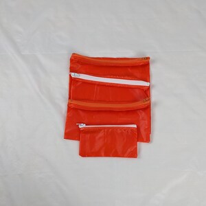 May include: Set of four orange zippered pouches, nested in size order. The pouches are made of a lightweight, water-resistant material.
