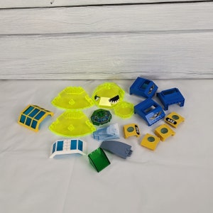 Puede incluir: Una colección de piezas de Lego en varios colores, incluyendo amarillo, azul, verde y blanco. Las piezas son principalmente curvas y tienen una variedad de formas y tamaños. Algunas de las piezas tienen detalles impresos, como números y símbolos.
