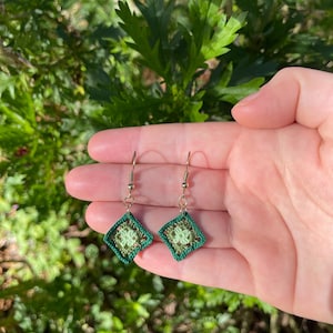 May include: A pair of green and light green crocheted earrings with gold hooks.