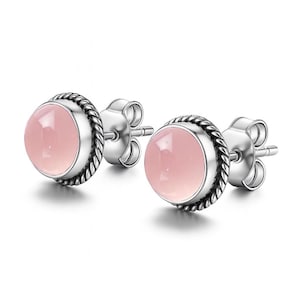 Puede incluir: Un par de pendientes de botón con piedras preciosas redondas de color rosa pálido engastadas en metal plateado. Los pendientes tienen un diseño de cuerda trenzada alrededor de la piedra preciosa, añadiendo textura y detalle.