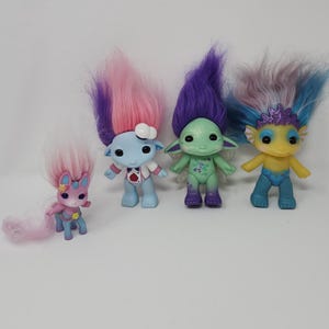 May include: A set of three ceramic mugs with a speckled, cream-colored glaze. Each mug features a different hand-painted design: a green leaf, a blue flower, and a yellow sun. The mugs have a simple, modern design.