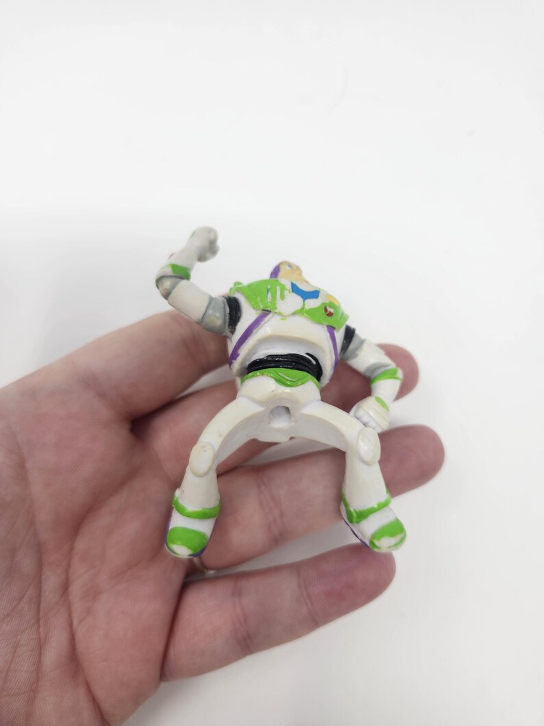 K&ouml;nnte beinhalten: Eine Buzz Lightyear Actionfigur, mit einem wei&szlig;en und gr&uuml;nen Raumanzug mit lila Akzenten. Die Figur ist mit einem erhobenen Arm posiert und zeigt das ikonische Design der Figur aus dem Film Toy Story.