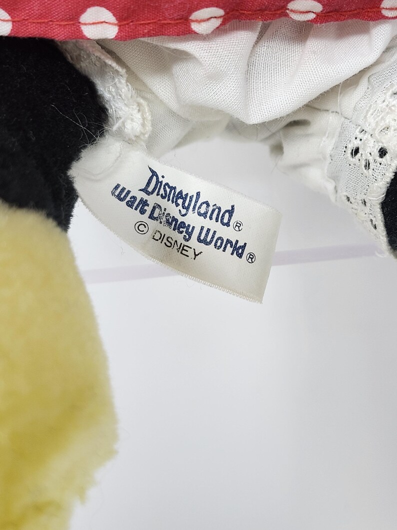 May include: A white tag with blue text that reads "Disneyland&reg; Walt Disney World&reg; &copy; DISNEY" attached to a red and white polka dot fabric.