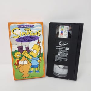 Può includere: Una scatola di videocassetta VHS arancione e una videocassetta VHS nera. La scatola recita "The Best Of The Simpsons" con personaggi dei cartoni animati e titoli degli episodi. La videocassetta VHS è etichettata "The Best Of The Simpsons Volume 5".