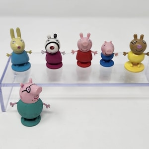 Puede incluir: Una colección de seis pequeñas figuras de plástico que representan varios animales con cuerpos redondeados y brazos extendidos. El conjunto incluye figuras en amarillo, morado, rojo, azul y verde azulado con rasgos faciales.