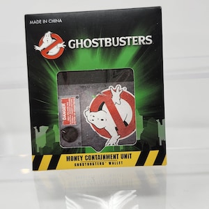 Op de afbeelding: Een zwarte Ghostbusters-portemonnee met een groen en geel stadslandschapontwerp. De portemonnee heeft het Ghostbusters-logo en de woorden "Money Containment Unit". De tekst "Made in China" is ook zichtbaar.