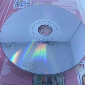 May include: A reflective silver CD-ROM disc in a pink and white case. The disc reflects a rainbow of colours. The case features the text "Scene" and images of cartoon characters. The disc is for a PC CD game.