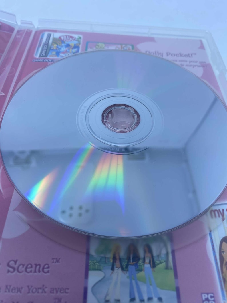 May include: A reflective silver CD-ROM disc in a pink and white case. The disc reflects a rainbow of colours. The case features the text "Scene" and images of cartoon characters. The disc is for a PC CD game.