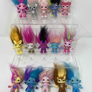 May include: A collection of colorful troll dolls with vibrant, long, fluffy hair. The dolls are in various colors, including pink, blue, yellow, and purple. Each doll has a unique facial expression and outfit. They are arranged on clear display shelves.