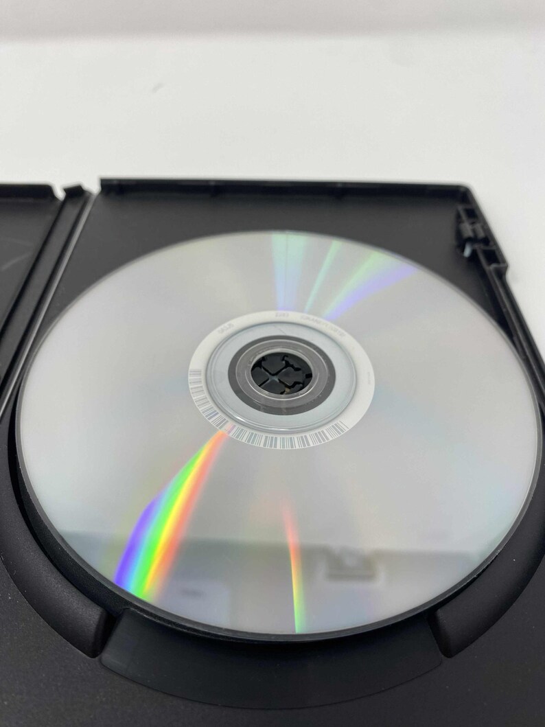 May include: A silver DVD disc inside a black plastic case. The disc reflects a rainbow of colors. The case is open, revealing the disc's surface and the surrounding black plastic.