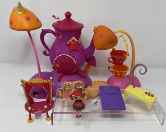 Może przedstawiać: Kolekcja kolorowych zabawek Lalaloopsy, w tym fioletowy domek w kształcie czajniczka, lalka, łóżko, stół i lampy w kształcie grzybów. Zabawki są w odcieniach różu, pomarańczy, żółci i fioletu, ze skomplikowanymi detalami.