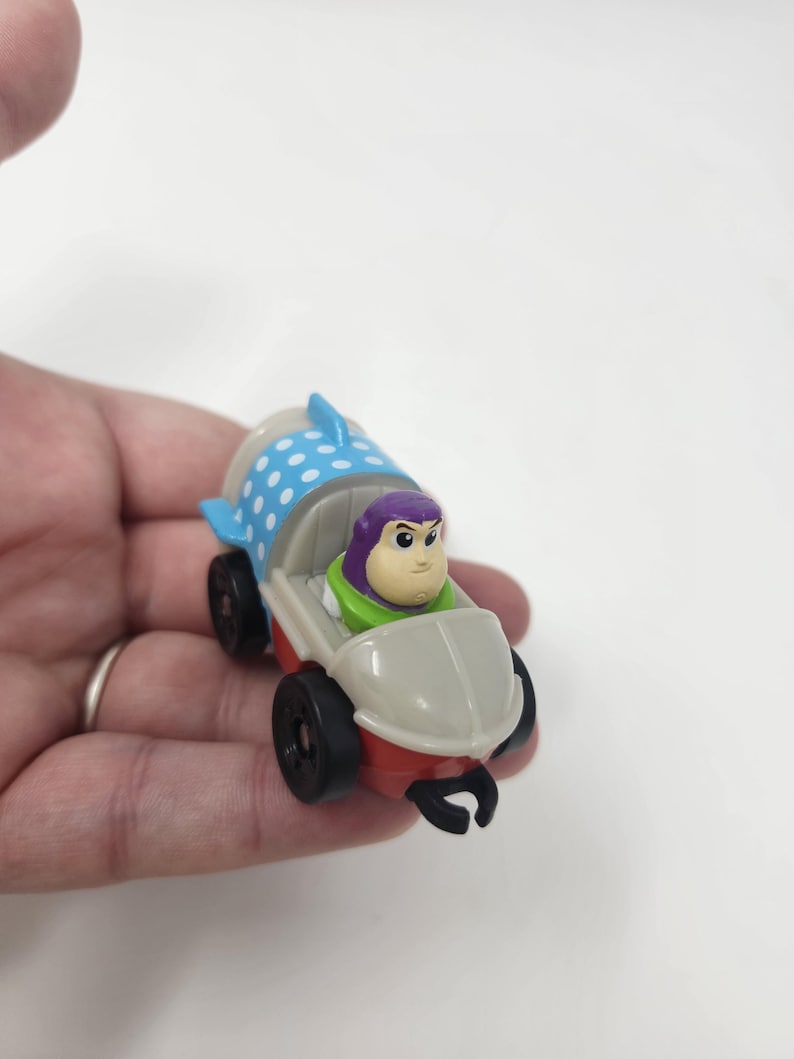 K&ouml;nnte beinhalten: Ein kleines Spielzeugauto mit Buzz Lightyear aus Toy Story. Das Auto hat einen roten und wei&szlig;en K&ouml;rper mit schwarzen R&auml;dern. Buzz Lightyear sitzt darin und tr&auml;gt seinen lila-gr&uuml;nen Raumanzug.