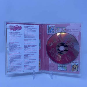 May include: A clear plastic case, open to reveal a Barbie Rapunzel CD-ROM. The CD is red and features the title "Rapunzel" and "My Scene". The case also contains printed inserts with French text.