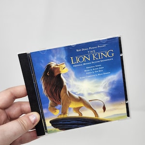 May include: The Lion King original motion picture soundtrack CD. The cover features a majestic lion against a blue sky background. The CD case has the text "Walt Disney Pictures Presents THE LION KING ORIGINAL MOTION PICTURE SOUNDTRACK".