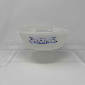 May include: A white, oval-shaped bowl with a blue and orange floral pattern around the rim. The bowl is made of a translucent material and sits on a clear, rectangular surface. The bowl is likely vintage.