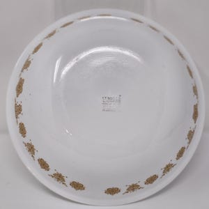 Peut inclure: Bol en céramique blanc avec un motif floral doré sur le bord. Le bol a un design simple et élégant, adapté pour servir des aliments. Le fond du bol contient du texte.