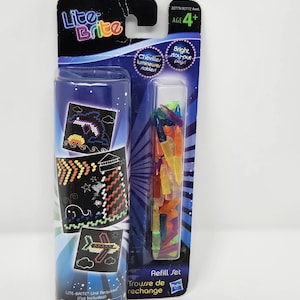 May include: A Lite-Brite refill set in its original packaging. The package includes a tube with example designs and a separate compartment with colorful pegs. The text on the package includes "Lite-Brite", "Refill Set", and a choking hazard warning.