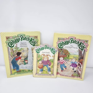 May include: Three vintage Cabbage Patch Kids storybooks. The books feature illustrations of children and the titles "Xavier's Fantastic Discovery", "Sybil Sadie", and "The Just-Right Family". The covers are yellow with green and pink accents.