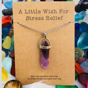 May include: A silver necklace with a purple crystal pendant. The card reads "A Little Wish For Stress Relief" and "Wear this pendant every day to bring tranquil energies your way."
