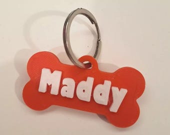 May include: Orange plastic dog tag shaped like a bone with a silver key ring. The tag has the name "Maddy" printed in white.