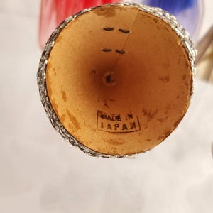 May include: A vintage, cone-shaped ornament with a silver glitter rim and the text "MADE IN JAPAN" stamped on the inside. The ornament has a natural, light brown interior and is likely part of a holiday decoration set.