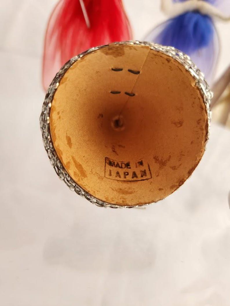May include: A vintage, cone-shaped ornament with a silver glitter rim and the text "MADE IN JAPAN" stamped on the inside. The ornament has a natural, light brown interior and is likely part of a holiday decoration set.