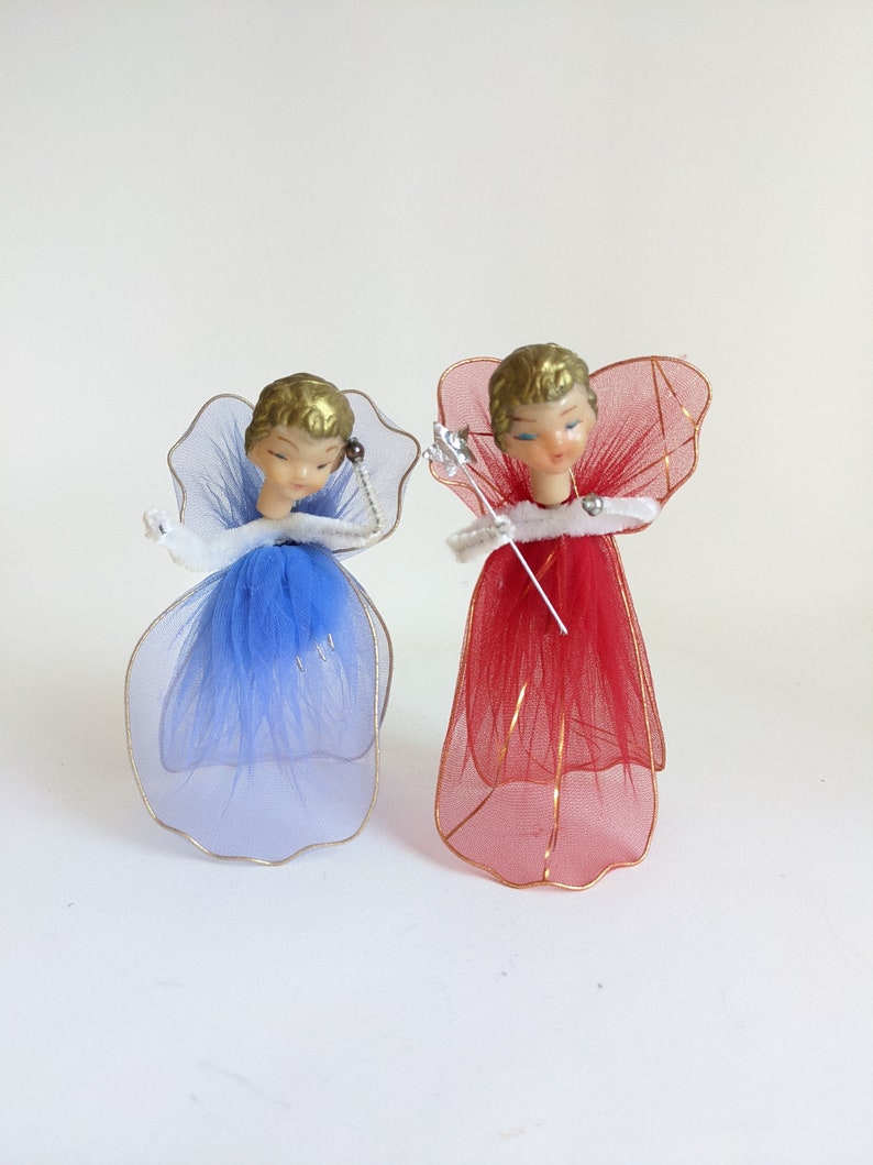 May include: Two vintage angel figurines. One angel has a blue tulle dress and wings, the other has a red tulle dress and wings. Both have gold hair and are holding a silver wand. The angels are Christmas tree ornaments.