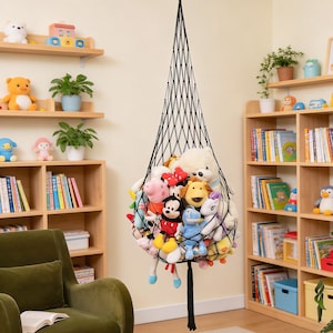 May include: A black mesh hanging storage net filled with various plush toys. The net is suspended from the ceiling, creating a space-saving solution for organizing stuffed animals. The toys are a mix of colors and characters.