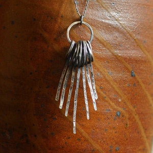 Puede incluir: Un collar de plata con un colgante hecho de múltiples círculos apilados y una franja de finos hilos de plata.