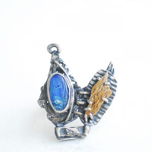 May include: A silver pendant with a blue oval stone set in a textured silver frame. The pendant also features a piece of wood with a natural grain pattern.