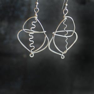 May include: A pair of silver earrings with a geometric design. The earrings are made of wire that is twisted and shaped into a series of overlapping circles and loops.