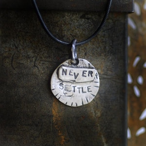 May include: A silver necklace with a round pendant that says "NEVER SETTLE" in a distressed font.
