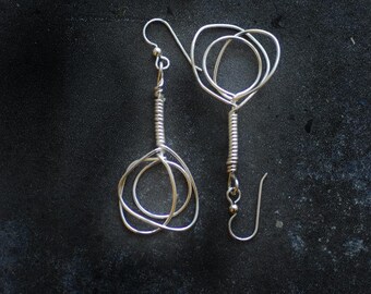 May include: A pair of silver wire earrings with a unique, abstract design. Each earring features multiple intertwined loops, creating a modern and geometric look.