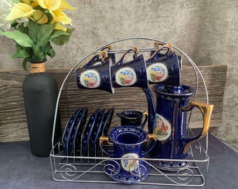 May include: A set of blue and gold teacups and teapot with floral designs on a metal rack. The cups and teapot have a blue and gold color scheme with floral designs. The rack is made of metal and has a decorative design.