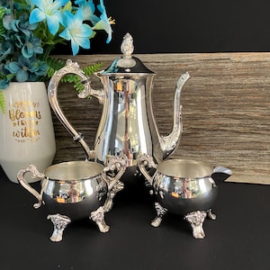 May include: A silver tea set comprising a teapot, creamer and sugar bowl. The set features a traditional design with ornate details and three legs.