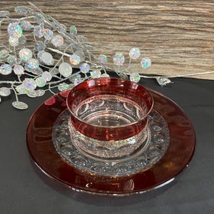 May include: A clear glass bowl with a red rim and a matching red glass plate. The bowl and plate have a decorative pattern.