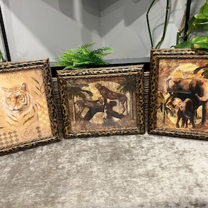 Op de afbeelding: Drie ingelijste dierendrukken met een luipaardprintlijst. De eerste print toont een tijger, de tweede een cheetah en de derde een olifant en een babyolifant.